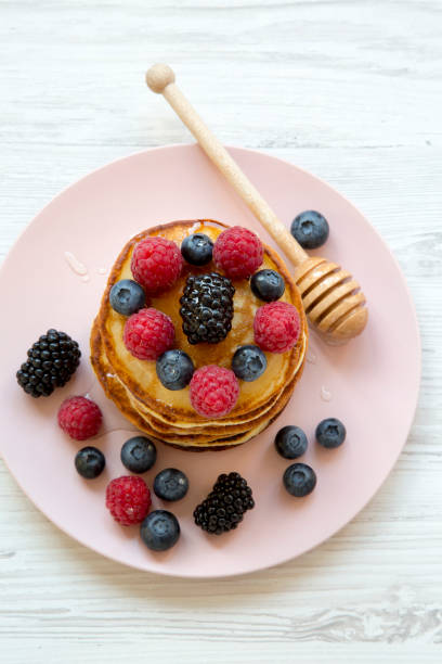 Delicious pancakes with berries and honey on a pink plate, top view. Close-up.