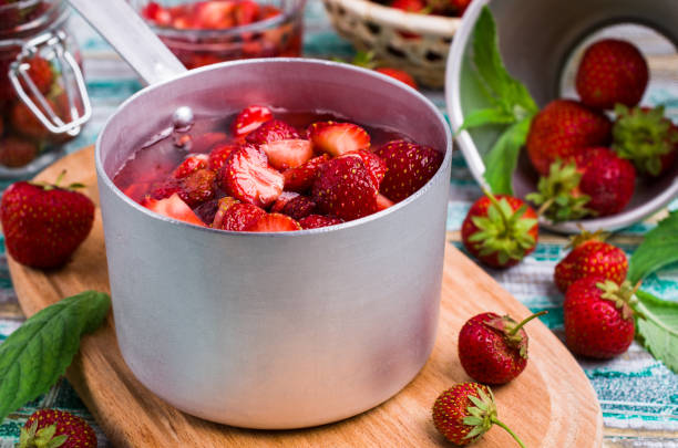Slices of red strawberries with syrup in a ladle on a wooden table. Selective focus.