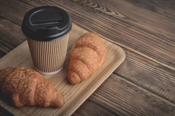 Two croissants and coffee-to-go on tray over wooden background