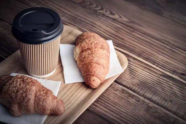 Two croissants and coffee-to-go on tray over wooden background