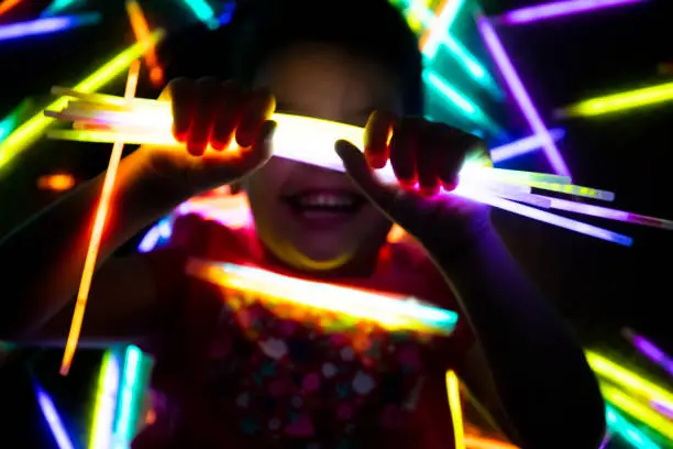 Photo of Cute little girl playing with glowsticks in her bedroom