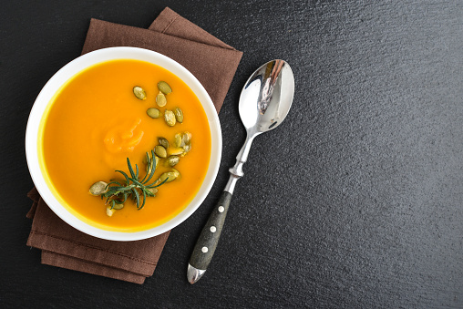 Pumpkin soup with seeds and spoon on grunge black slate background, top view