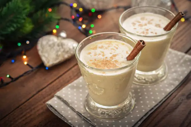 Traditional christmas drink eggnog in glass with spices and  christmas lights on wooden background