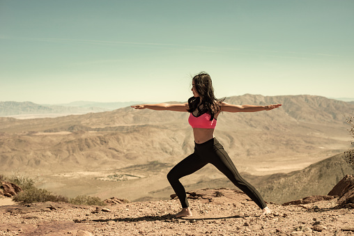 A beautiful Hispanic women doing yoga on a mountain ridge with the desert below.