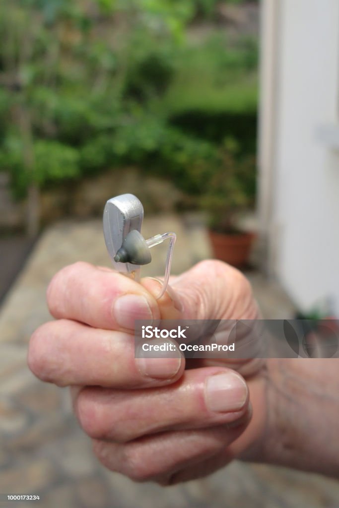 closeup hand Man holding hearing aid on blurred background Close-up Of senior Man Hand Holding Hearing Aid AIDS Stock Photo