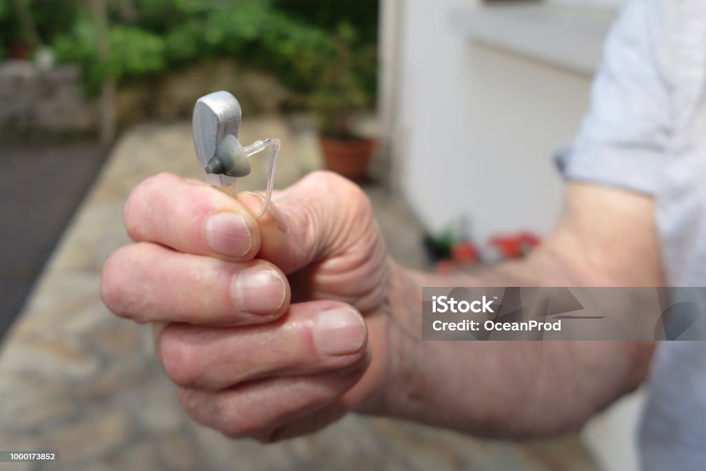 Close-up Of senior Man Hand Holding Hearing Aid closeup hand Man holding hearing aid on blurred background AIDS Stock Photo