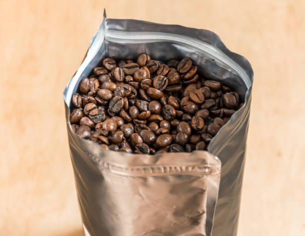 istock Coffee beans in a plastic foil package on wooden background. 1000237852
