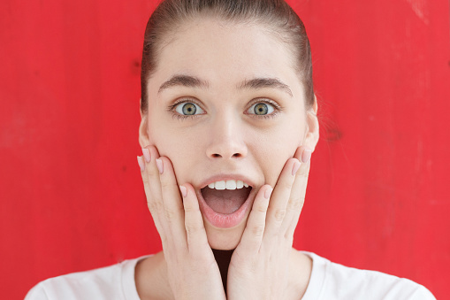 Are you kidding me? Oh my god! Wow! Really? Crazy shocked young girl, looking at camera with wide opened mouth and bugged eyes, standing against bright red background