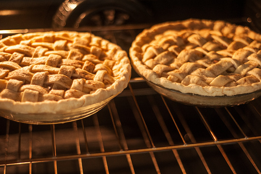 Two homemade apple pies baking in an oven on the top rack.  Horizontal image.