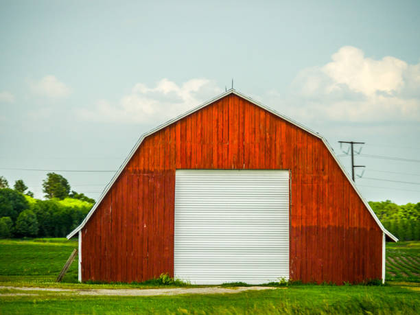 Beautiful photograph of a freshly painted red vintage weathered wood barn with pitched roof in a field with blue sky and white fluffy clouds above. stock photo