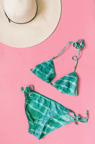 istock Aquamarine bikini swimsuit and straw hat arranged on light pink background. 1000409912