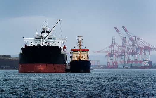 Loading grain into holds of sea cargo vessel in seaport from silos of grain storage. Bunkering of dry cargo ship with grain. Aerial top view