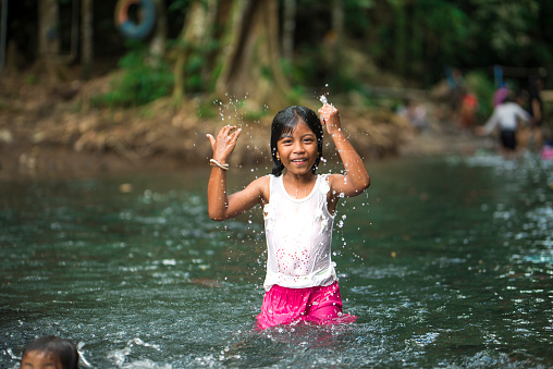 Cute little Indonesian girl splashing the water in a river.