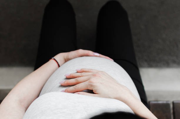 Top view of pregnant woman sitting outside and huging her belly.