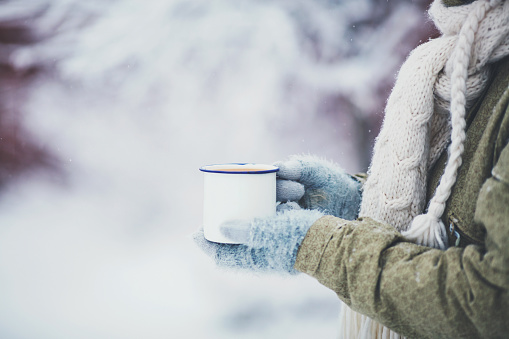 Female hands holding cup of hot drink in snowy weather