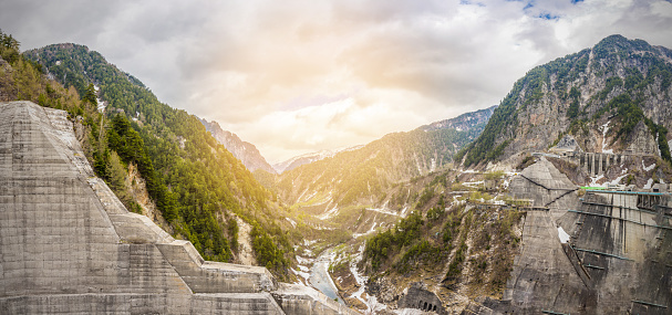 Panorama Beautiful scenery of Kurobe Dam on a brisk, with colorful lakeside mountains and crystal clear lake water under blue sunny sky in Tateyama Kurobe Alpine Route, Toyama, Japan