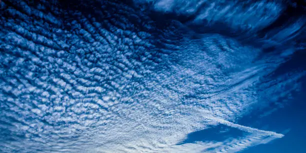 A spectacular inspirational brightly coloured atmospheric cloudy sky cloudscape featuring a Cirrocumulus cloud formation in a mid blue sky. New South Wales, Australia.