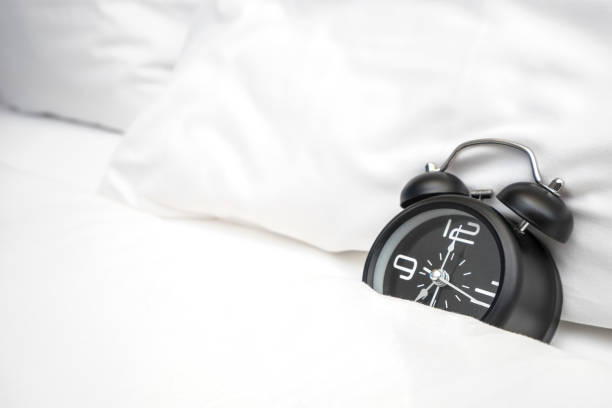 istock Analog alarm clock is on white bed, Time in the morning with a bright sunshine 1000681004