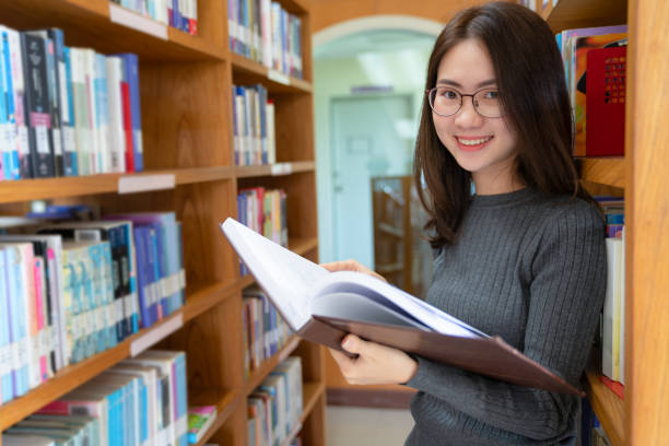 istock Back to school education knowledge college university concept, Beautiful female college student holding her books smiling happily standing in library, Learning and education concept 1000681356