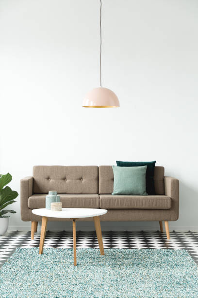 istock Front view of a sofa with pillows, coffee table, chandelier and green carpet set on a white wall 1000697238