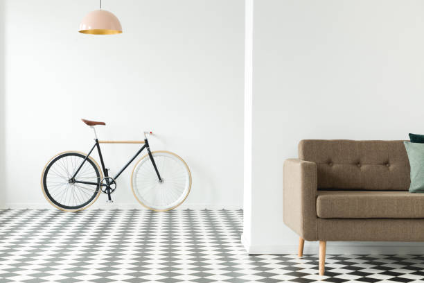istock Bike on an empty wall, cropped sofa in front and checkered floor in an anteroom interior 1000697304