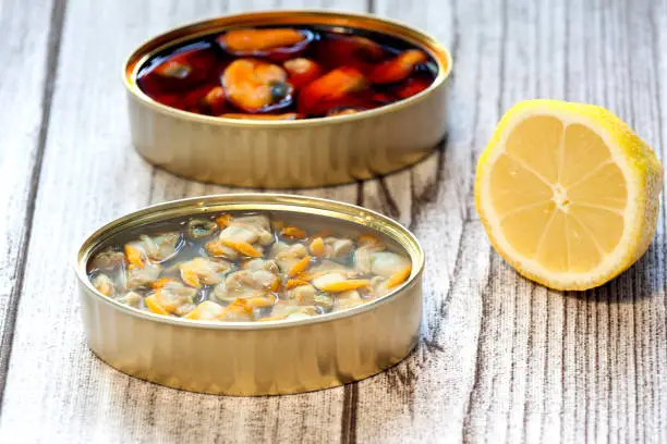tin pickled mussels, tin can cockles and lemon slice on wood background