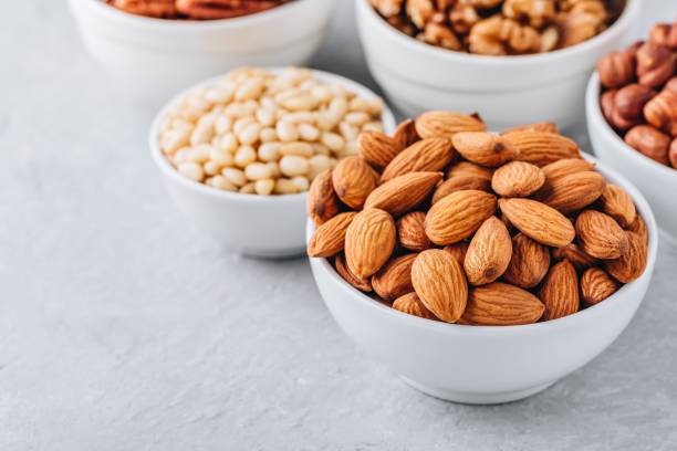 istock Almonds, pecans, walnuts, pine nuts and hazelnuts in white bowls on grey background. Assortment of nuts. 1000710174