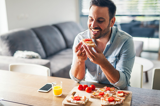 Hungry young man eating sandwich at home