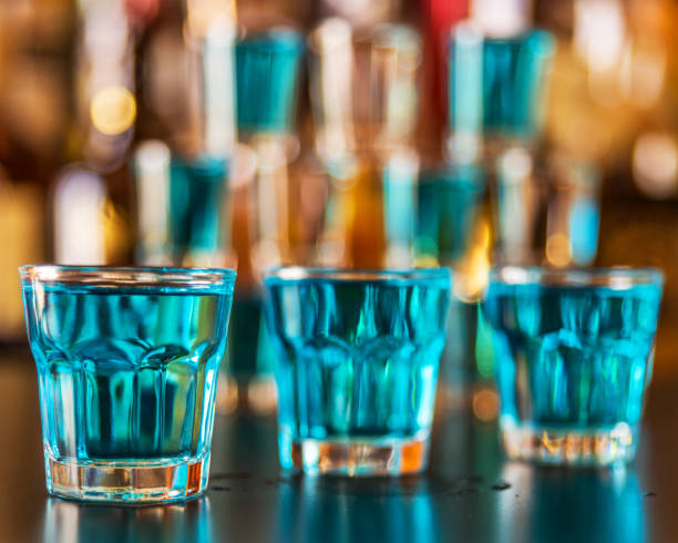 популярный голубой напиток расстрелял камикадзе на фоне бара с бутылками, освежающим напитком - kamikaze cocktail drink lemon стоковые фото и изображения