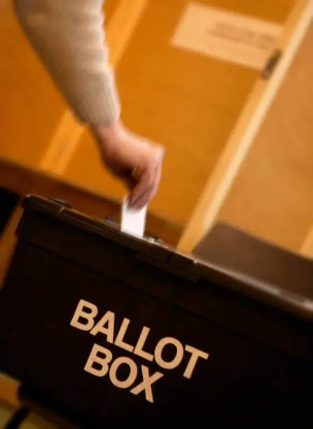 HAND PLACING VOTING SLIP INTO BLACK BALLOT BOX IN CLOSE UP