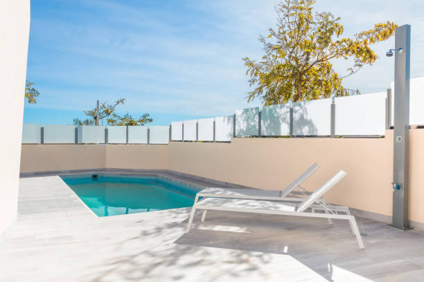istock Swimming pool with turquoise water, next to two white deck chairs, in the background a blue sunny sky. 1000761104