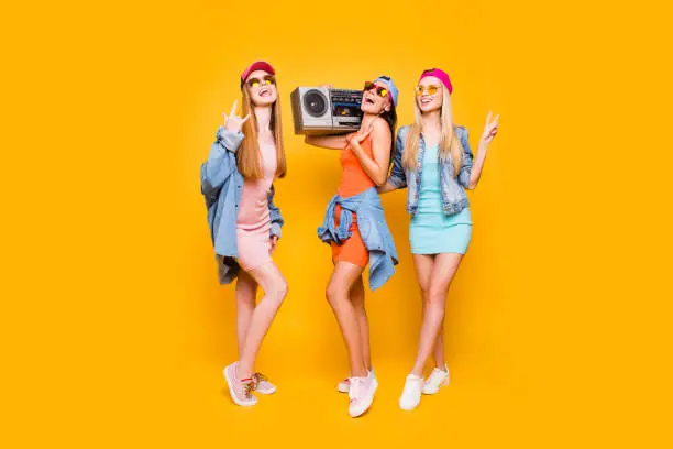 Photo of Rock-and-roll sneakers jeans eyewear peace symbol leisure rest relax concept. Portrait of funky trio having stereo audio player enjoying time together isolated on vivid yellow background