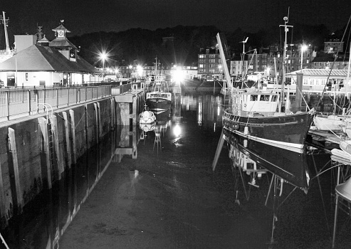 Black and white shot of fishing boats moored in Rothesay harbour next to the pier at night. July 5th, 2015
