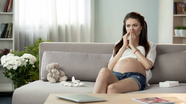 sick pregnant woman blowing stuffy nose in tissue, feeling bad, cought cold - cought imagens e fotografias de stock