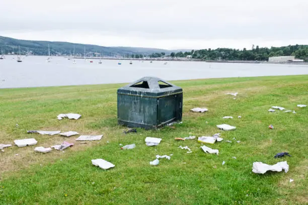 Photo of litter garbage rubbish in park outside of bin lying on ground green grass ruin view seaside resort uk