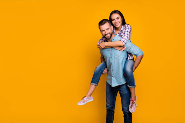 istock Advertisement concept. Portrait with copy space empty place of handsome man carrying on back pretty woman looking at camera isolated on vivid yellow background 1000822854