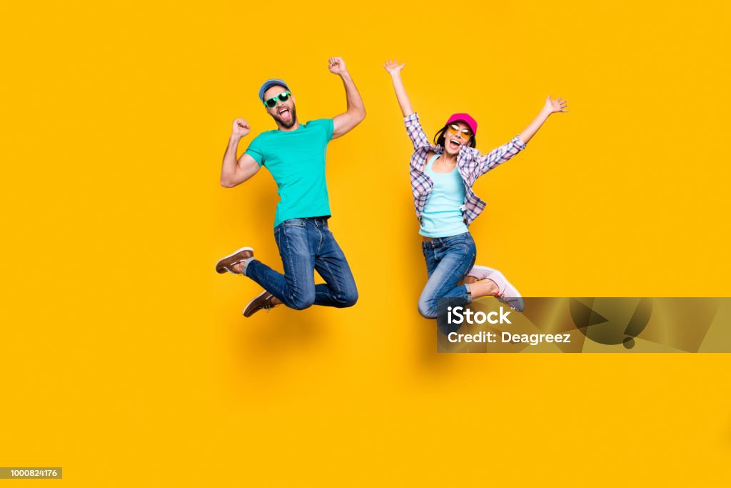 Portrait of lucky successful couple jumping with raised fists celebrating victory wearing denim outfit isolated on bright yellow background. Energy luck success concept Jumping Stock Photo