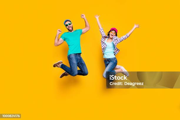 Portrait Of Lucky Successful Couple Jumping With Raised Fists Celebrating Victory Wearing Denim Outfit Isolated On Bright Yellow Background Energy Luck Success Concept Stock Photo - Download Image Now