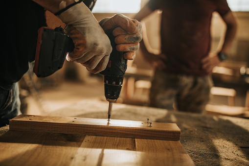 Close up of unrecognizable carpenter using drill while working on furniture in a workshop.
