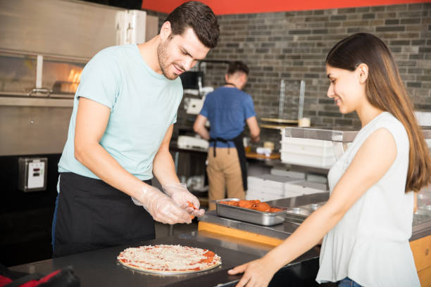 istock Handsome chef cooking pepperoni pizza and adding ingredients on top 1000839014