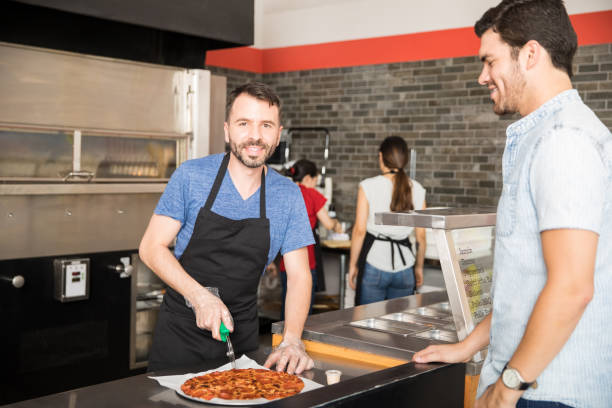 Smiling chef cutting pizza slices at counter in front of customer