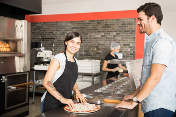 istock Smiling chef woman preparing pizza for customer standing behind counter in kitchen 1000842348