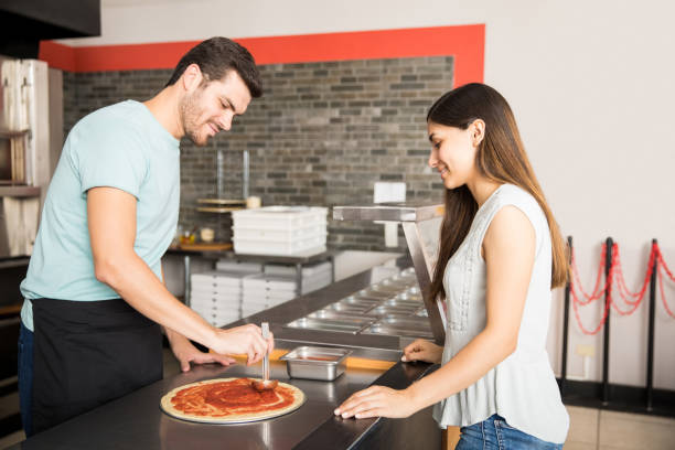 istock Smiling customer looking at chef applying tomato puree on pizza bread 1000842444