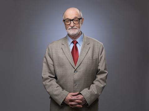 Portrait of handsome senior man in suit on gray background with copy space