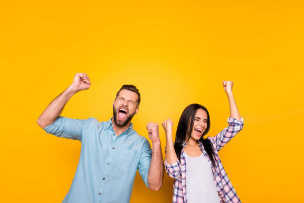 portrait d’un homme fou couple plein de bonheur hurlant bruyamment tenant bras levés, gardant les yeux fermés célébrant victoire isolé sur fond jaune vif - human fist photos et images de collection