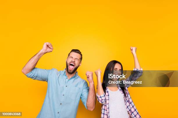 Portrait Of Crazy Man Couple Full Of Happiness Yelling Loudly Holding Raised Arms Keeping Eyes Closed Celebrating Victory Isolated On Vivid Yellow Background Stock Photo - Download Image Now