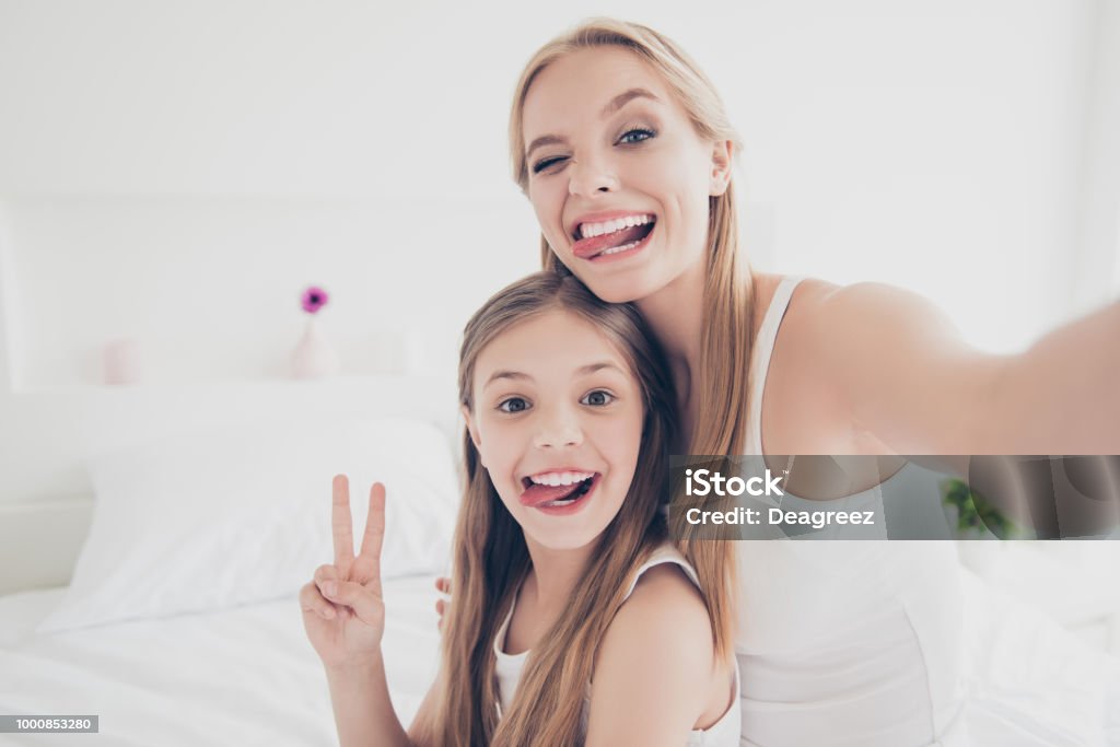 Indoors domestic lifestyle grimace fooling concept. Close up portrait of cute cool funky funny beautiful pretty excited rejoicing delightful mom and offspring making taking self picture in bed room Mother Stock Photo