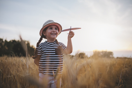 Gorgeous little toddler girl with a hat, playing in meadow with her airplane model.
