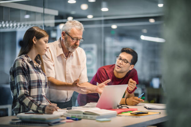 istock Mature teacher explaining a lecture to his students while using laptop at campus. 1000868386