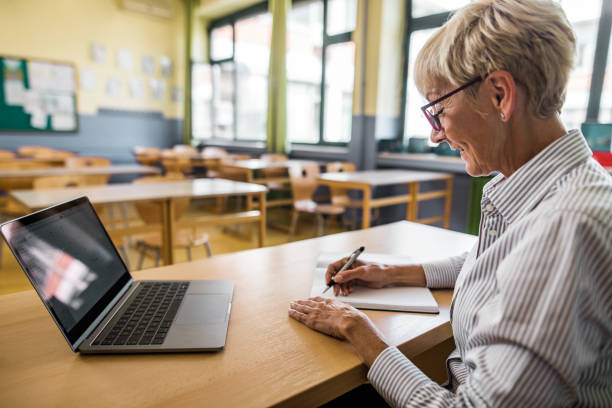 istock Smiling senior teacher taking notes in the classroom. 1000878052